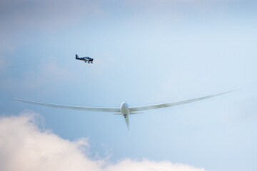 a small plane and a glider sailplane flying over white clouds on a blue sky