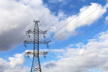 High voltage tower with electrical wires on background of blue sky with white clouds. Electricity transmission lines, power supply concept