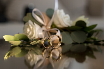 Close up of two wedding gold rings on mirror table with bouquet of white roses