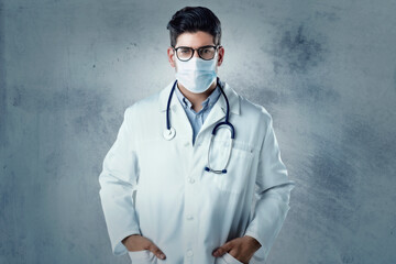 Portrait of male doctor wearing face mask for prevention while standing at isolated background