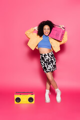 full length of african american woman posing with boombox on pink