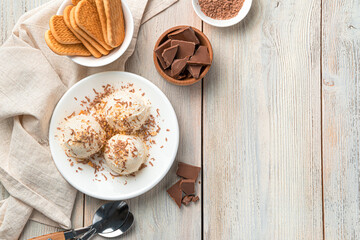 Three balls of ice cream with chocolate chips and cookie crumbs in a white plate on a light background.