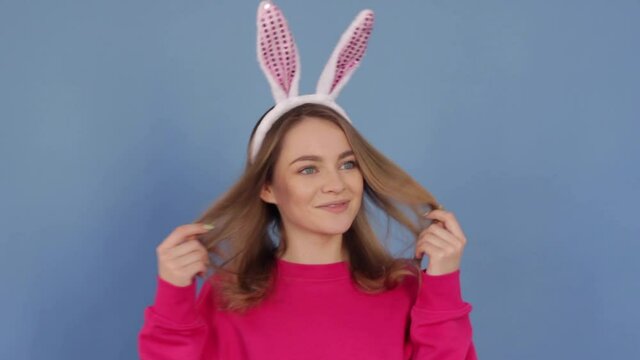 Young beautiful woman of Caucasian ethnicity in bunny ears smiles cutely and shows different emotions on a pastel blue background. Close-up