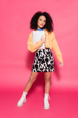 full length of curly african american woman posing with laptop on pink