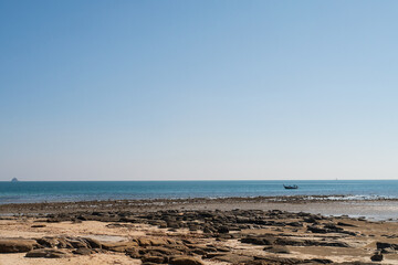 Nature background of rocky seashore beach wave and coastline, clear blue sky with cloud, and sunlight water surface for holiday relaxation lifestyle landscape concept