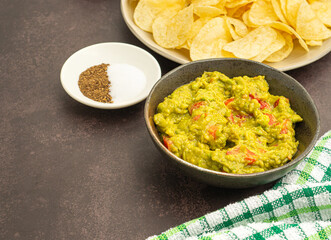 Fresh guacamole and crispy potato chips on a plate placed on dark brown background with copy space for text. Top view. Concept of traditional Mexican foods and healthy fruits