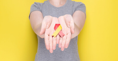 World Hepatitis Day concept. Girl in gray T-shirt holds in her hands awareness symbol red-yellow ribbon. Yellow background