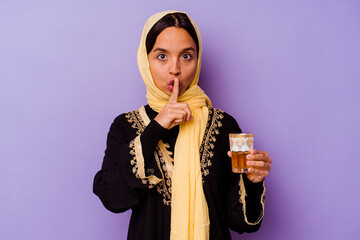Young Moroccan woman holding a glass of tea isolated on purple background keeping a secret or asking for silence.