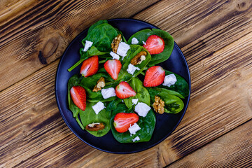 Salad with spinach leaves, feta cheese, walnuts and strawberry on a black plate. Top view