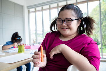 Young girls disabilities Or Down's syndrome learning about drawing shape and orange color painting with bright smile for active learning and encouraging beside. Education and special child concept.