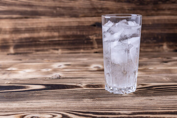 a glass of fresh seltzer water with ice on a wooden background. space for text