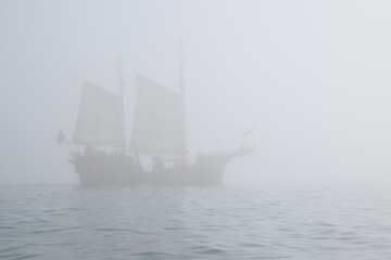 Fisherman is sitting on a sandy cliff with his fishing rod, a person is fishing in a foggy day at the ocean, leisure and hobby time 