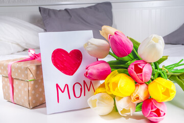 Mother's day, daughter's day holiday concept lifestyle. Preschooler child toddler blonde girl with a bouquet of tulip flowers, handmade greeting card and gift box copy space