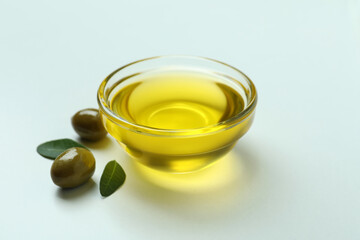 Bowl of oil, olives and leaves on white background
