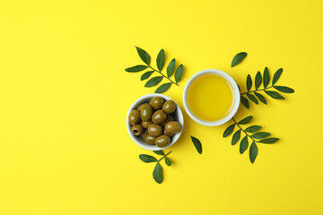 Bowls of oil and olives, and twigs on yellow background
