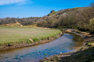 Fototapeta na wymiar A view looking back along Pennard Pill stream towards the castle ruins, Gower Peninsula, Swansea, South Wales on a sunny day