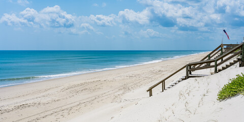 Naklejka premium Wooden stairs to the beach by the ocean from a private house and a weather vane with the symbols of the American flag