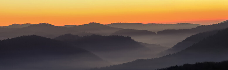 foggy, misty valley with orange sky before sunrise, beautiful orange yellow lighted sky