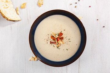 Celery cream soup in dark plate on white rustic background from above.