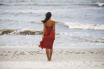Fototapeta na wymiar Woman in a Red on the Beach, Cold Windy Weather