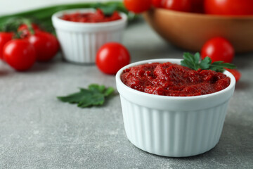 Bowls with tomato paste on gray background with ingredients