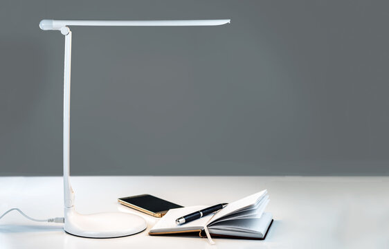 A smartphone and open diary with a pen on the table under the desktop LED lamp.