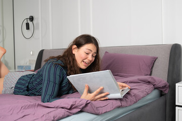 Happy woman lying on a bed. she watches photo album or reading a book. High quality photo