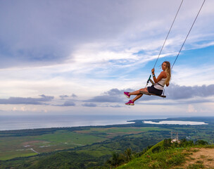 A young girl, blonde, swinging on a swing on a mountain slope in summer.