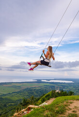 A young girl, blonde, swinging on a swing on a mountain slope in summer.