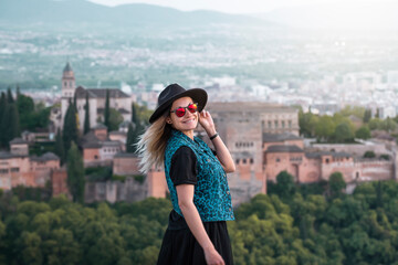 A young female traveler with sunglasses and casual style contemplates the views of the Alhambra palace in the city of Granada, Spain