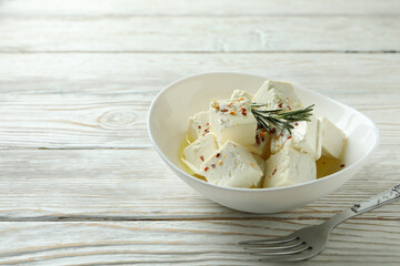 Bowl with feta cheese and fork on white wooden background