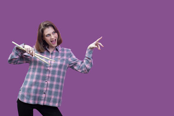 young beautiful girl, musician, holding drum sticks in hands. In a plaid shirt on a pink background