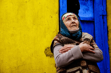An elderly woman in a poor area. Grandmother on a yellow background. The old grandmother in the background of the slums. Helping vulnerable populations. Poverty and disadvantage concept. Grandmother - obrazy, fototapety, plakaty
