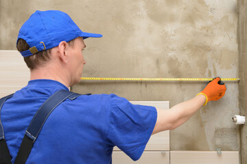 The master tiler measures the distance on the wall with a tape measure