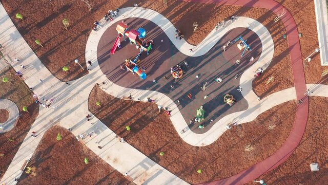 Playground For Kids In A Park Bustling With Activity, Busy With Children Having Fun And Playing On Merry-go-round, Slide, Playhouse And Swing, Enjoying Sunny Afternoon Casting Long Shadows.  Top View.