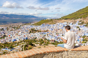 Fototapeta na wymiar European man traveler creates a trip route and receives information about traveling using digital tablet of the town of Chefchaouen, Morocco.