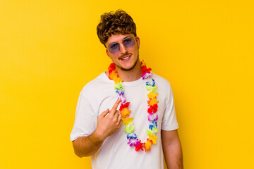 Young caucasian man wearing a Hawaiian party stuff isolated on yellow background pointing with...
