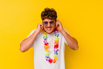Young caucasian man wearing a Hawaiian party stuff isolated on yellow background covering ears with...