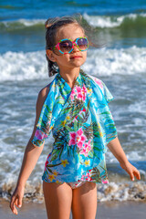 Little girl in a blue scarf on a background of the sea. Baby in sunglasses on a background of waves and sky