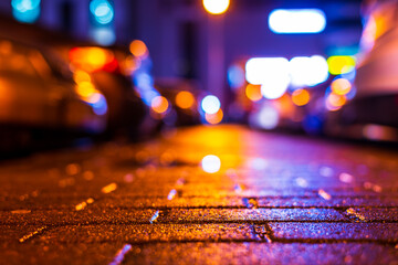 Rainy night. Parking mall with cars. Reflections of shop windows on the wet pavement. Colorful colors. Close up view from the pavement level.