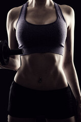 Slim athletic woman Holding dumbbell in the hand on black