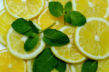 halves and slices of fresh juicy bright yellow lemons with mint leaves, spread out as a background, taken close-up