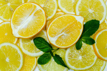 halves and slices of fresh juicy bright yellow lemons with mint leaves, spread out as a background, taken close-up