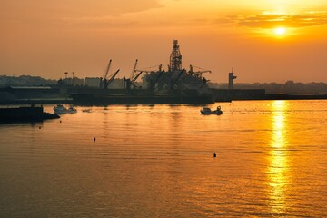 Fototapeta premium scene of fishing boats entering port at dawn with harbor cranes, an oil platform and the city skyline in the background