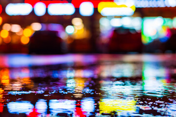 Rainy night. Parking mall with cars. Reflections of shop windows on wet asphalt. Colorful colors. Close up view from the level of the puddle on the asphalt