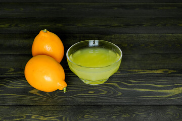 two juicy ripe lemons and a glass cup with lemon juice on a dark, coarse wooden background made of boards
