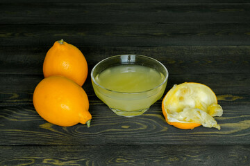 two juicy ripe lemons, a squeezed lemon peel and a glass cup with lemon juice on a dark, coarse wooden background made of boards
