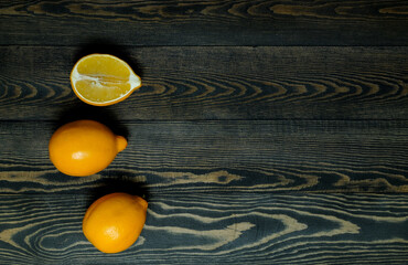 two whole lemons and one half lemon on a dark, coarse wooden background from boards