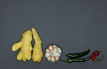 two roots of juicy fresh ginger, garlic head, sharp red and green peppers on a gray background, photographed close-up