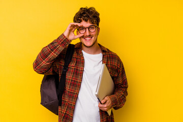 Young student caucasian man holding a laptop isolated on yellow background excited keeping ok...
